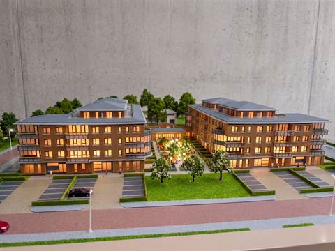 Maquette van twee appartementengebouwen met verlichte ramen, een binnentuin en parkeerplaatsen