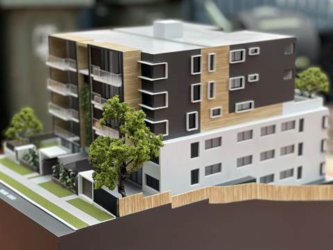 Maquette van een appartementengebouw met houten gevelaccenten en een boom op de voorgrond